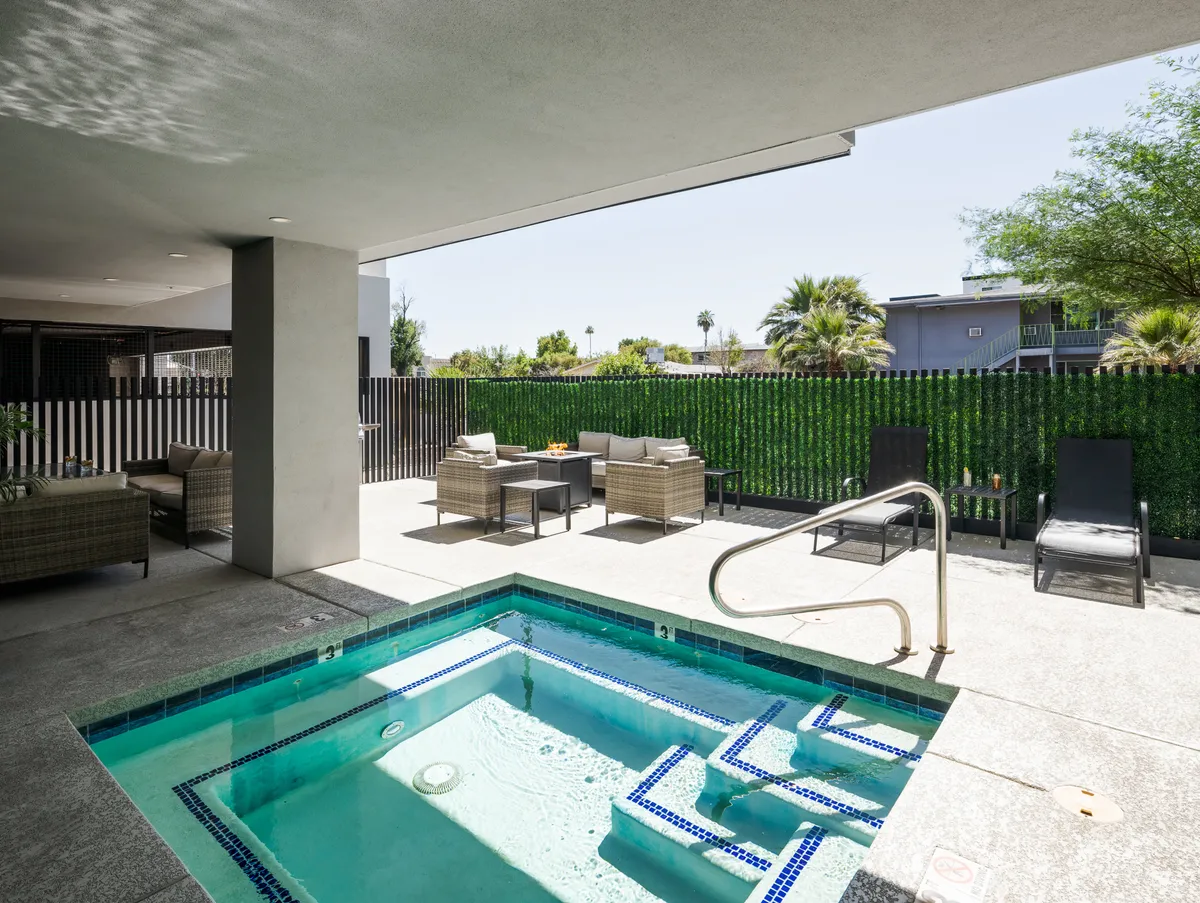 A welcoming exterior scene featuring a glistening swimming pool surrounded by lush greenery and comfortable seating areas. The pool is accented by the warm glow of sunset, suggesting opportunities for socializing, sunbathing, and enjoying evening barbecues in a resort-style shared outdoor space.