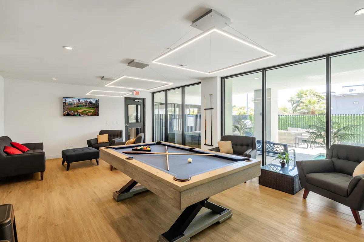 A vibrant interior shot of the community clubhouse featuring a pool table, large television, and a casual seating area. The scene conveys a social, inviting atmosphere designed for friendly competitions and group gatherings.