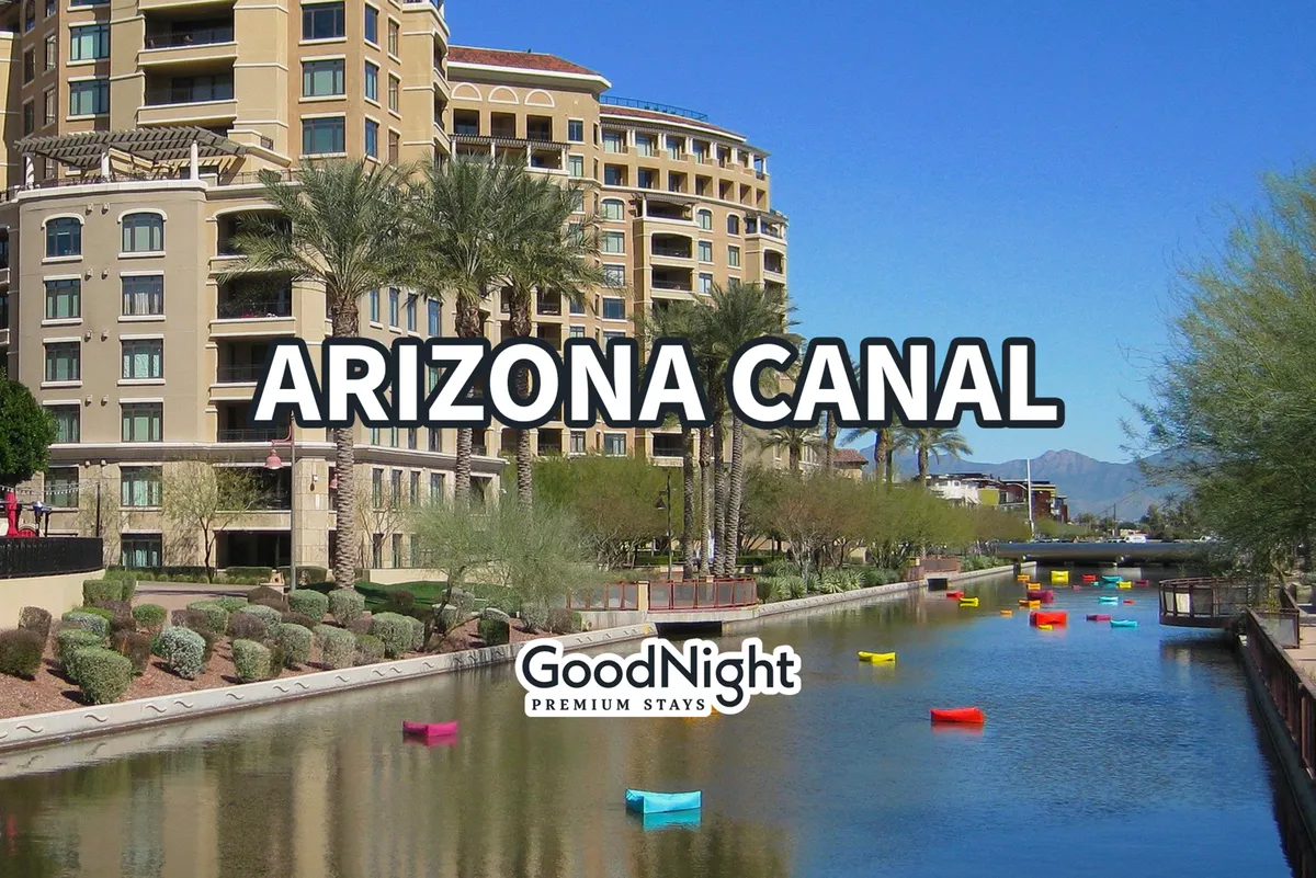 A picturesque exterior shot of the Arizona Canal lined with palm trees and modern architecture, colorful boats on the water, and people leisurely strolling along the canal. The lively atmosphere hints at vibrant local events and easy access to nearby shops.