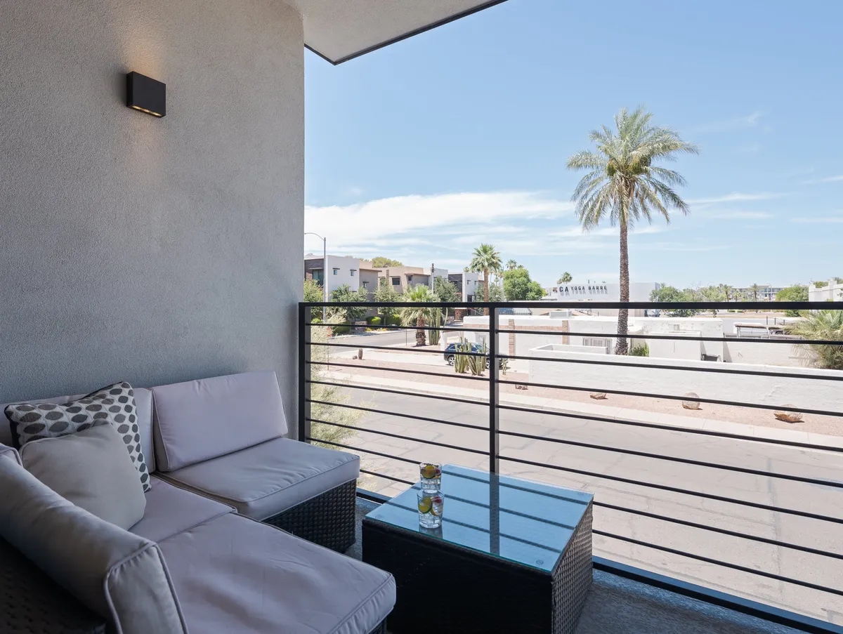 An inviting outdoor seating area shaded by a palm tree, with an urban view of Scottsdale beyond. The area is designed for relaxation and socializing, perfect for enjoying drinks and sunsets while being close to the city's vibrant life.
