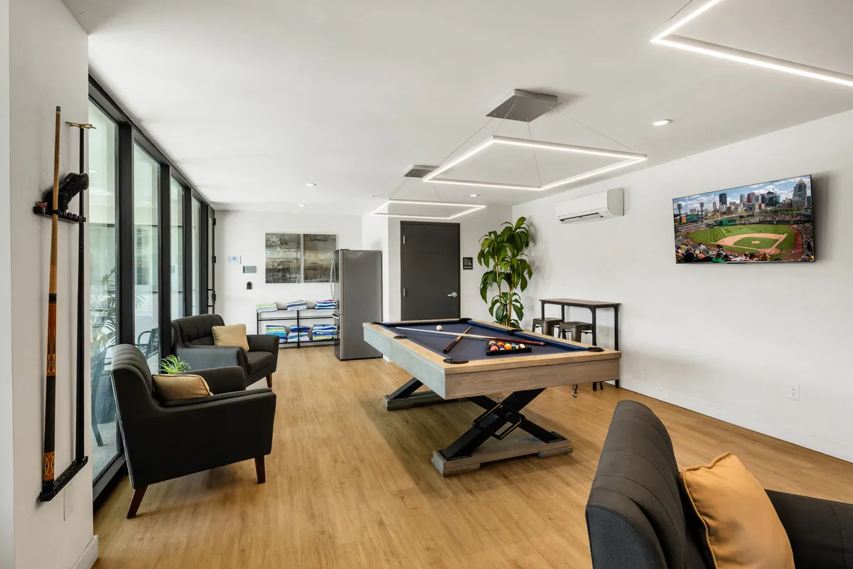 A lively interior community room equipped with a pool table, comfortable seating area, and a television. The room is set up for entertainment, games, and social gatherings, reflecting a fun and casual atmosphere ideal for group stays.